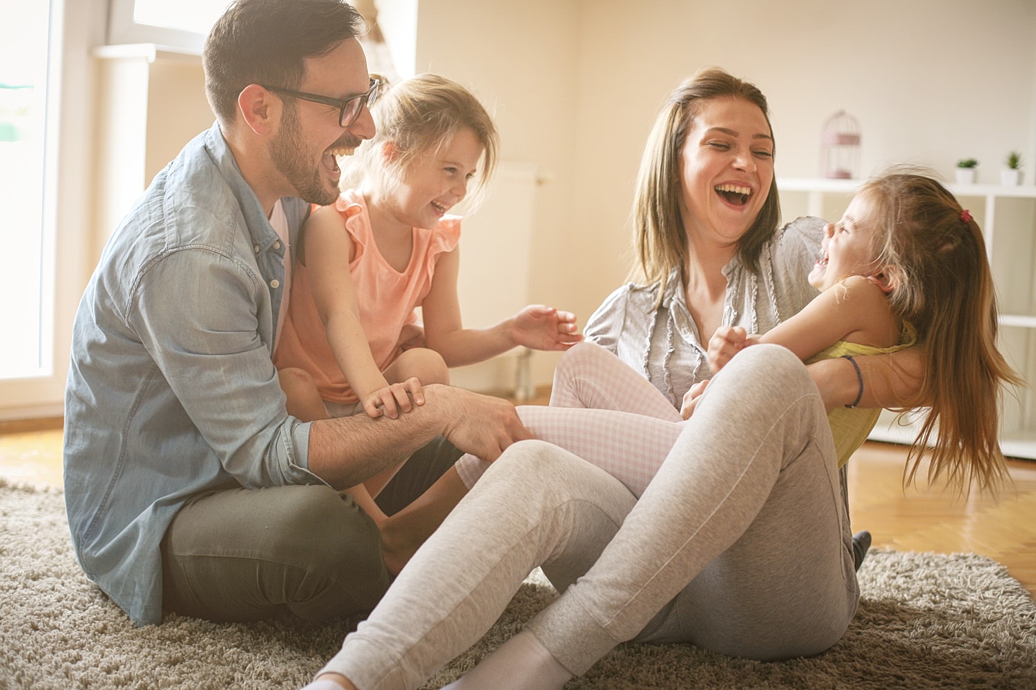 Family playing and laughing on living room carpet.