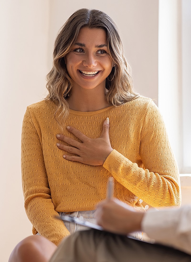 Smiling woman in yellow sweater, engaged in conversation.