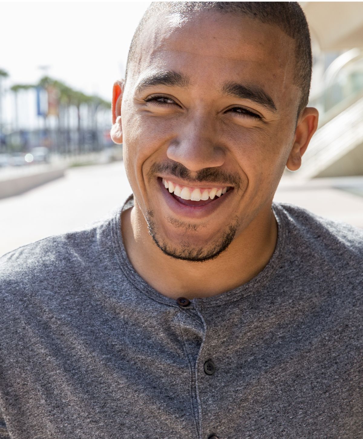 Smiling man wearing a gray shirt outdoors.