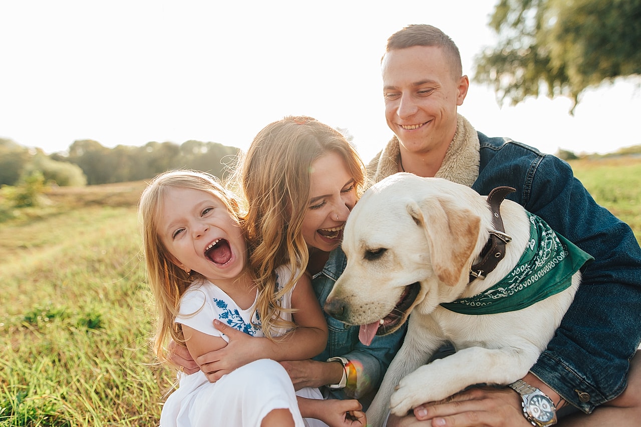 Family enjoying time with a happy dog in a green field.