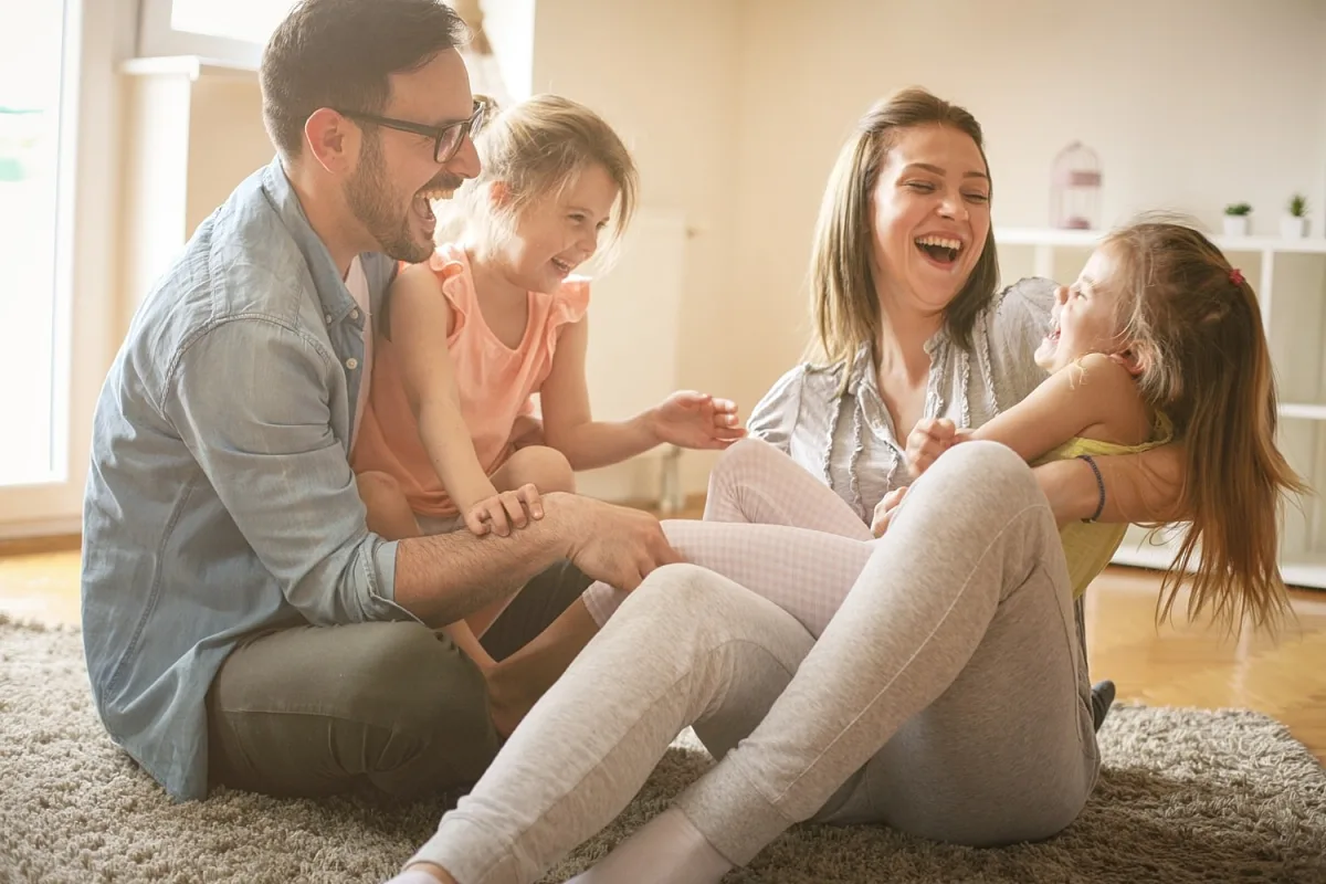 Family playing and laughing on living room carpet.