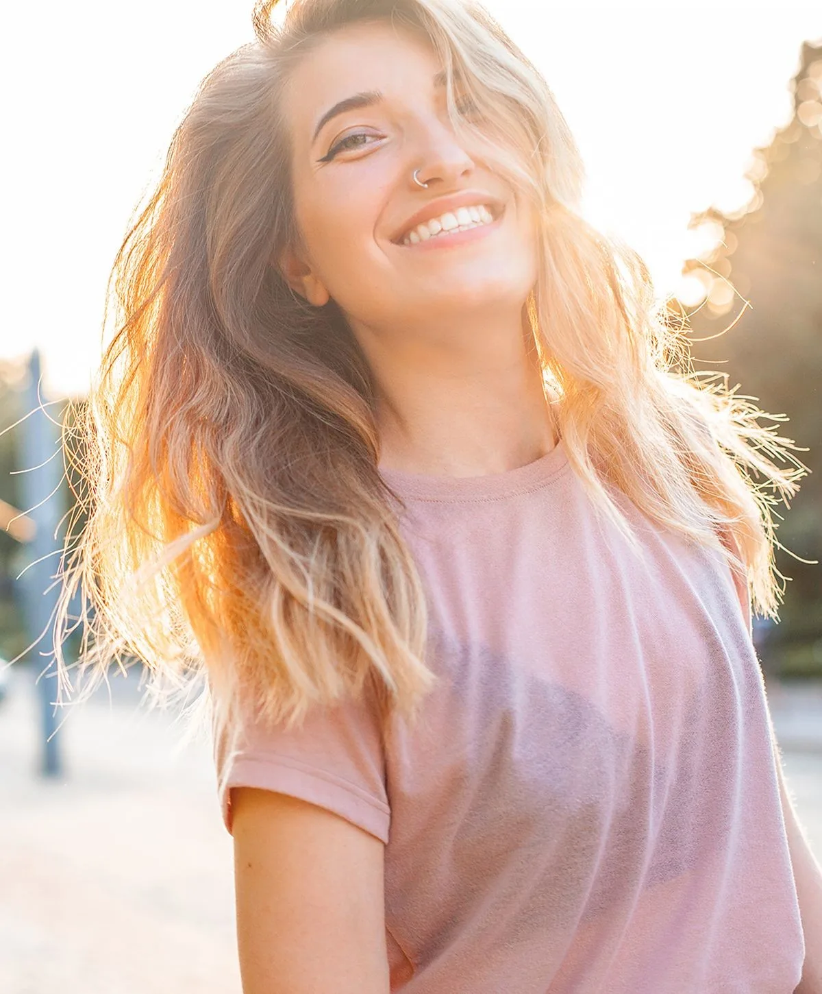 Smiling woman with sunlit, wavy hair outdoors.