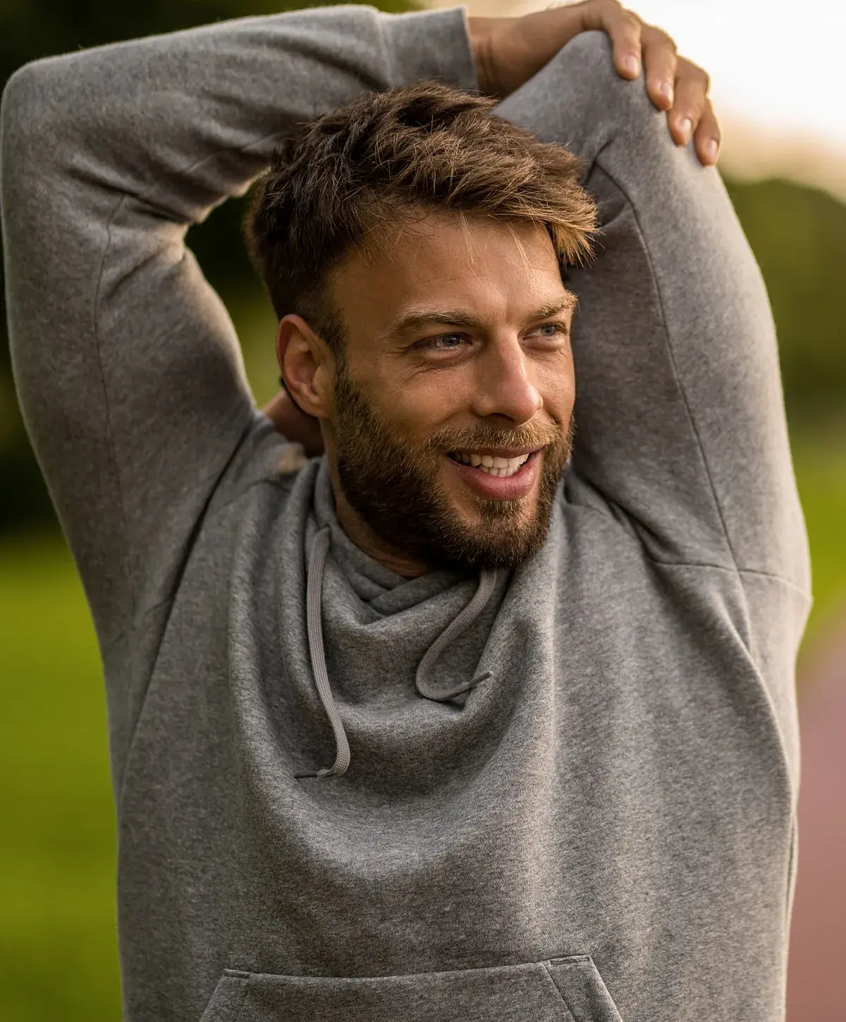 Man stretching outdoors in a grey hoodie.