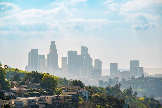 Los Angeles skyline and surrounding hillside neighborhoods under a blue sky.