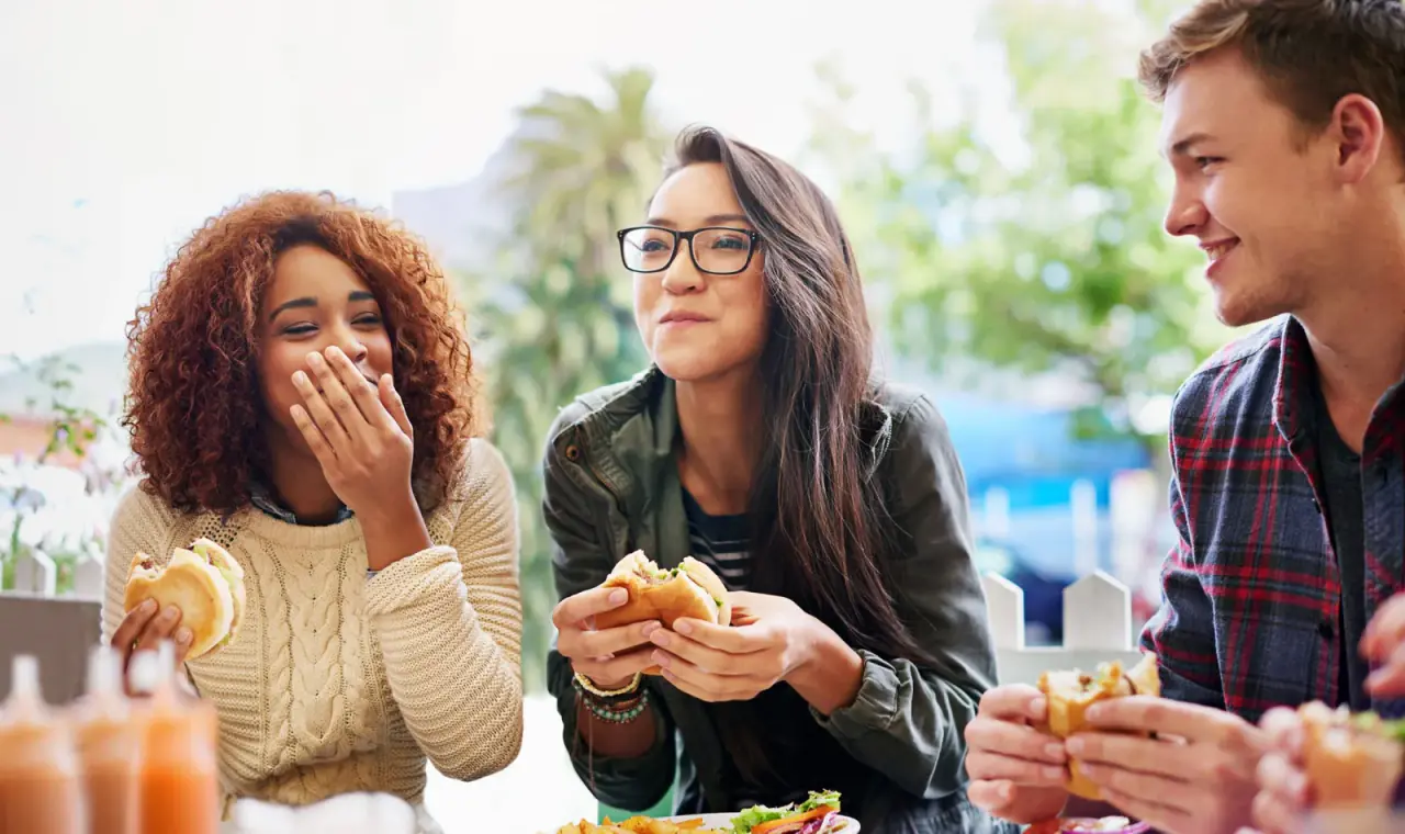 Friends enjoying burgers and laughing together outdoors.