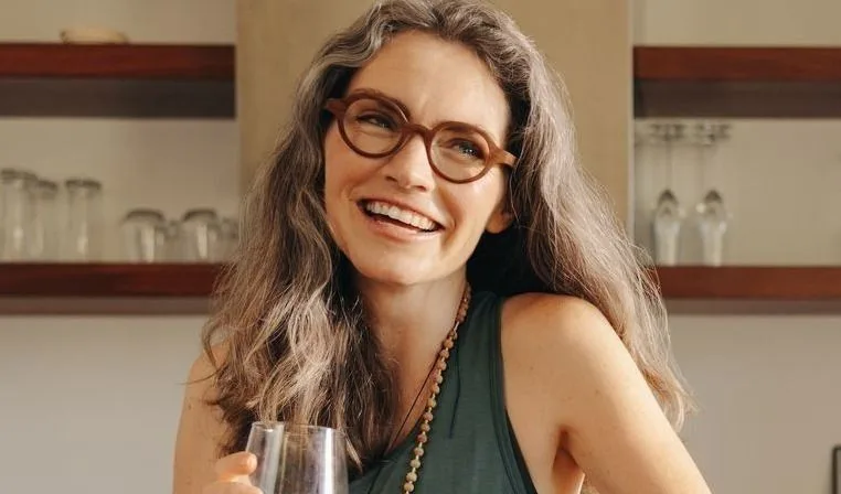 Smiling woman with glasses holding a drink.