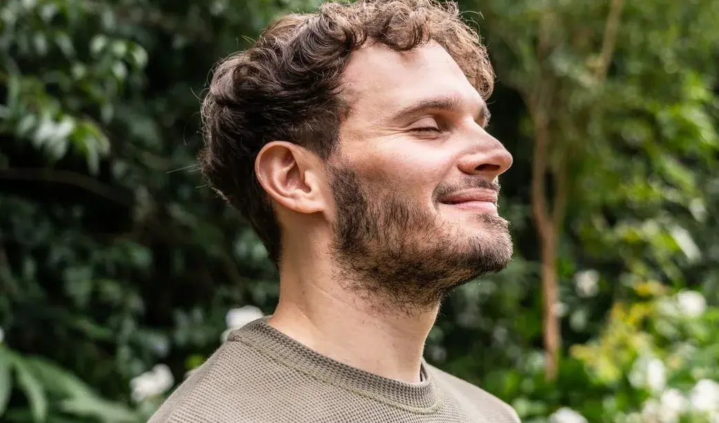 Smiling man enjoying nature with eyes closed.