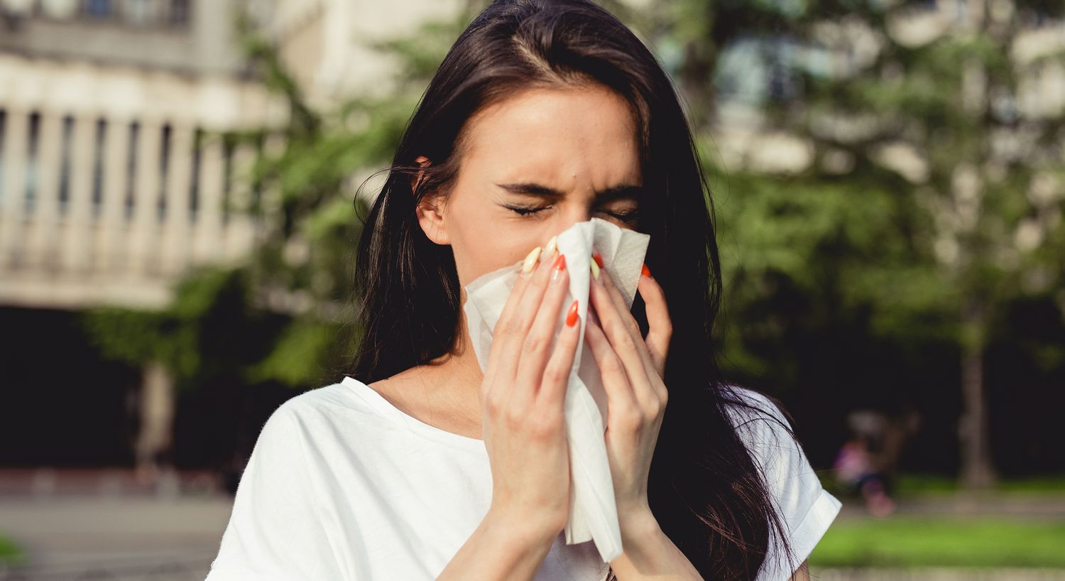 Woman sneezing and holding a tissue outdoors.